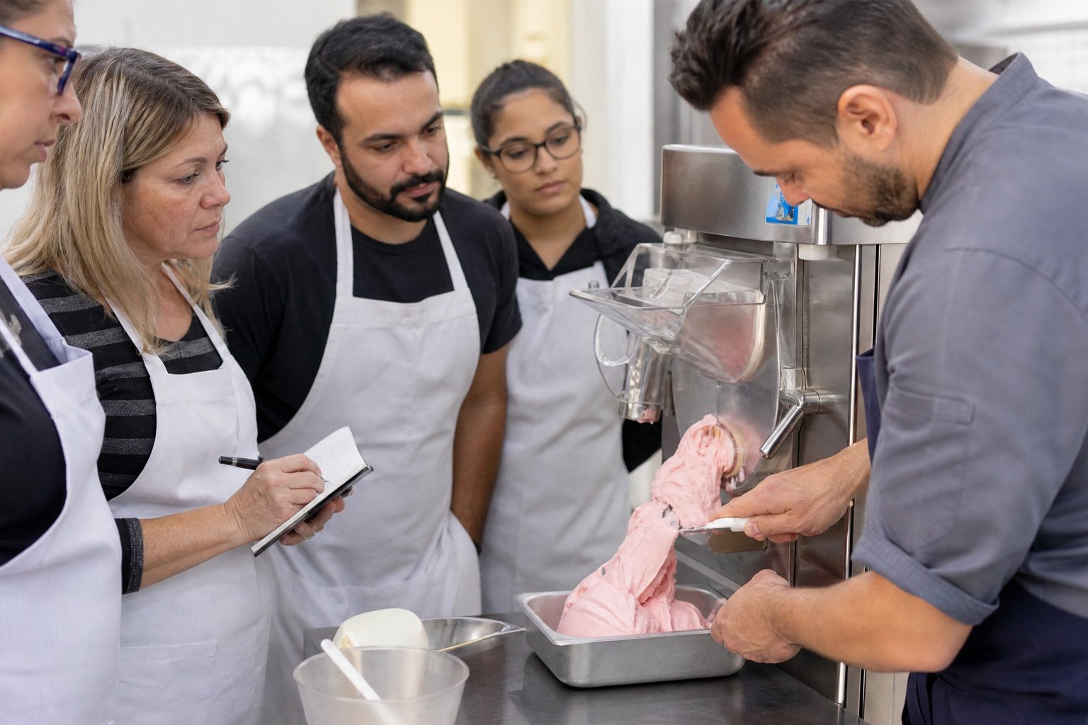 Grupo aprendendo a técnica de balanceamento de sorvete em um curso prático de sorveteria
